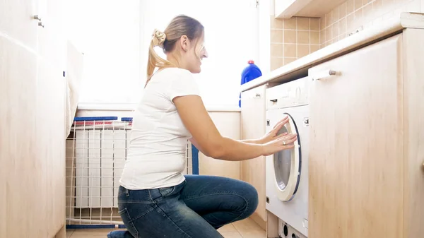 Schöne junge Hausfrau schließt Tür der Waschmaschine in der Wäscherei — Stockfoto