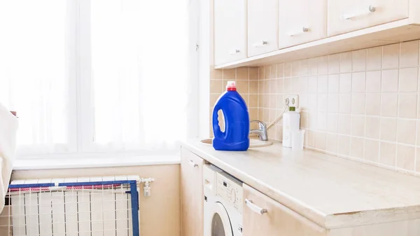 Stor flaska flytande tvättmedel stående på bord vid tvätt i hus — Stockfoto