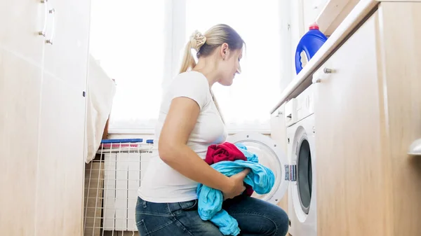 Beautiful young housewife taking clothes out of washing machine in laundry — Stock Photo, Image