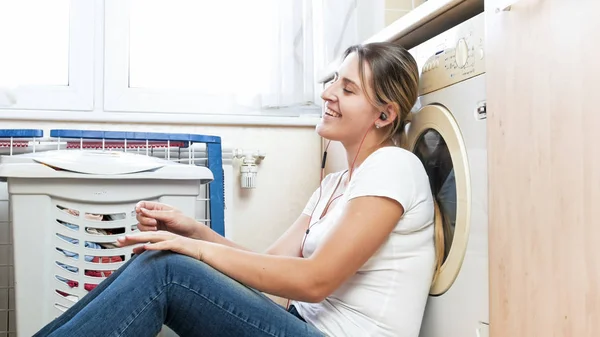 Portret van gelukkige jonge vrouw luisteren muziek met koptelefoon terwijl u wacht voor wasgoed — Stockfoto