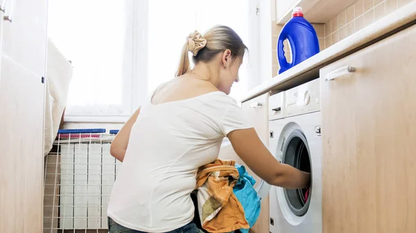 Jeune femme au foyer blonde chargement de vêtements sales dans la machine à laver — Photo