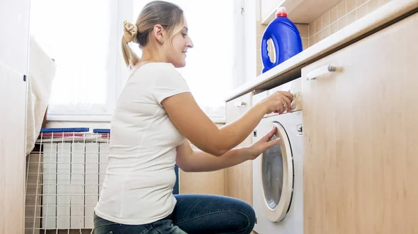 Portrait of smiling young housewife setting program on washing machine — Stock Photo, Image