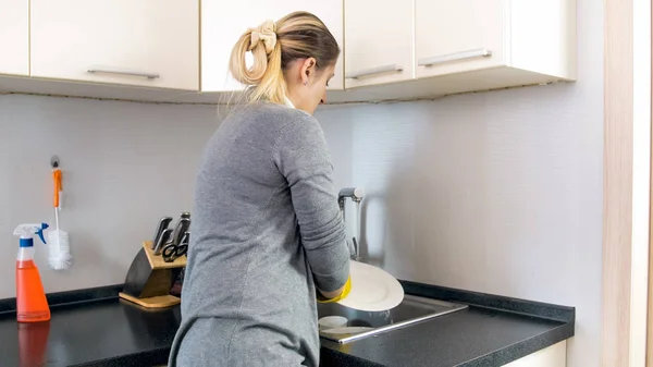 Δείτε τη φωτογραφία πίσω νεαρή γυναίκα το πλύσιμο των πιάτων στο νεροχύτη της κουζίνας — Φωτογραφία Αρχείου