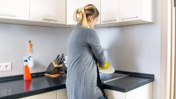 Citra tampilan belakang ibu rumah tangga muda dalam mencuci piring sarung tangan di wastafel — Stok Foto