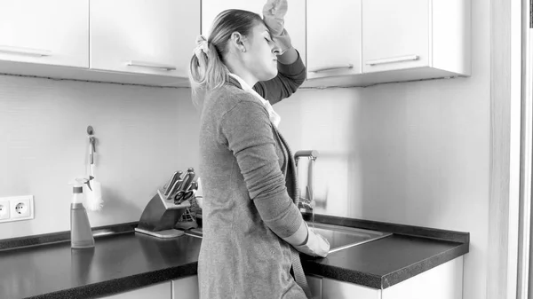 Donna stanca in bianco e nero che lava i piatti in cucina — Foto Stock