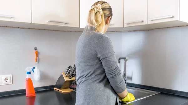 Foto von hinten: junge Hausfrau steht an Küche und spült Geschirr — Stockfoto