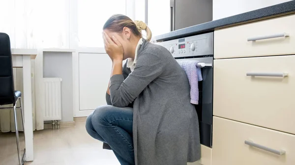 Jonge huisvrouw zittend op de vloer in de keuken te huilen — Stockfoto