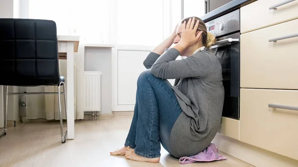 Wanita muda frustrasi duduk di lantai dapur — Stok Foto