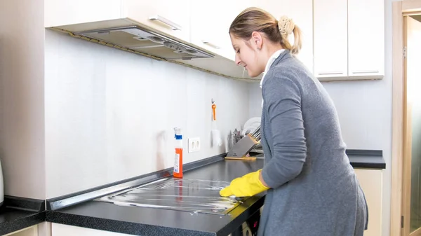 Mooie jonge huisvrouw reiniging elektrische kookplaat op keuken — Stockfoto