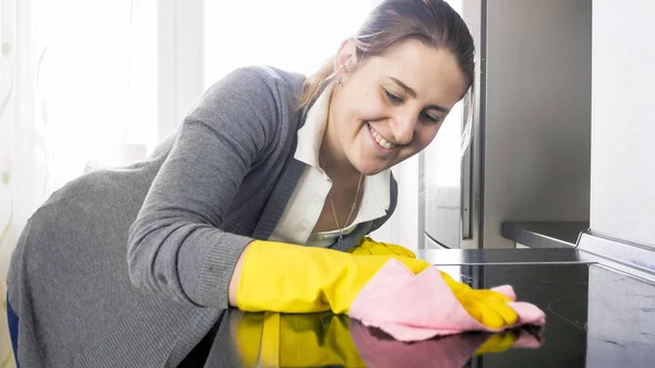 Mulher sorridente bonita limpando sujo manchado placa elétrica na cozinha — Fotografia de Stock