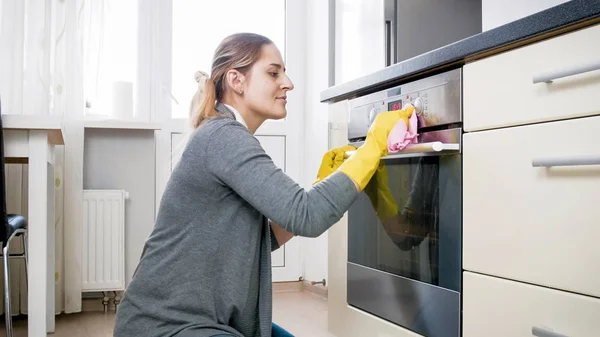 Cantik tersenyum wanita dengan kain membersihkan noda dari oven — Stok Foto