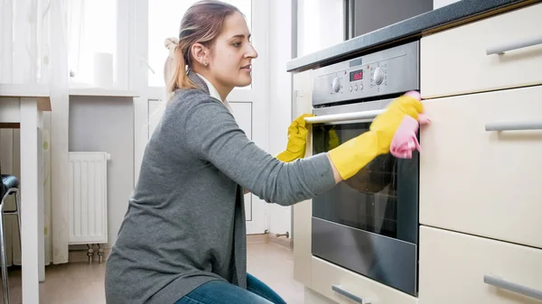 Schöne junge Frau putzt befleckten Ofen mit Tuch — Stockfoto