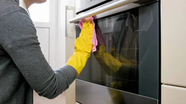 Foto close-up wanita muda dengan sarung tangan kuning mencuci pintu oven kaca kotor — Stok Foto