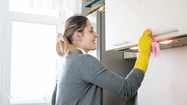 Portrait of young smiling woman washing cupboard and cabinets on kitchen