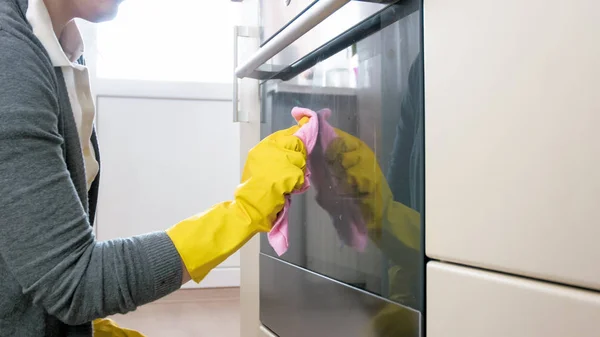 Foto close-up wanita menghilangkan kotoran dan noda di pintu oven setelah memasak — Stok Foto