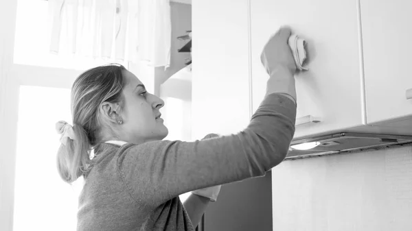 Retrato preto e branco de jovem dona de casa lavar armários de cozinha — Fotografia de Stock