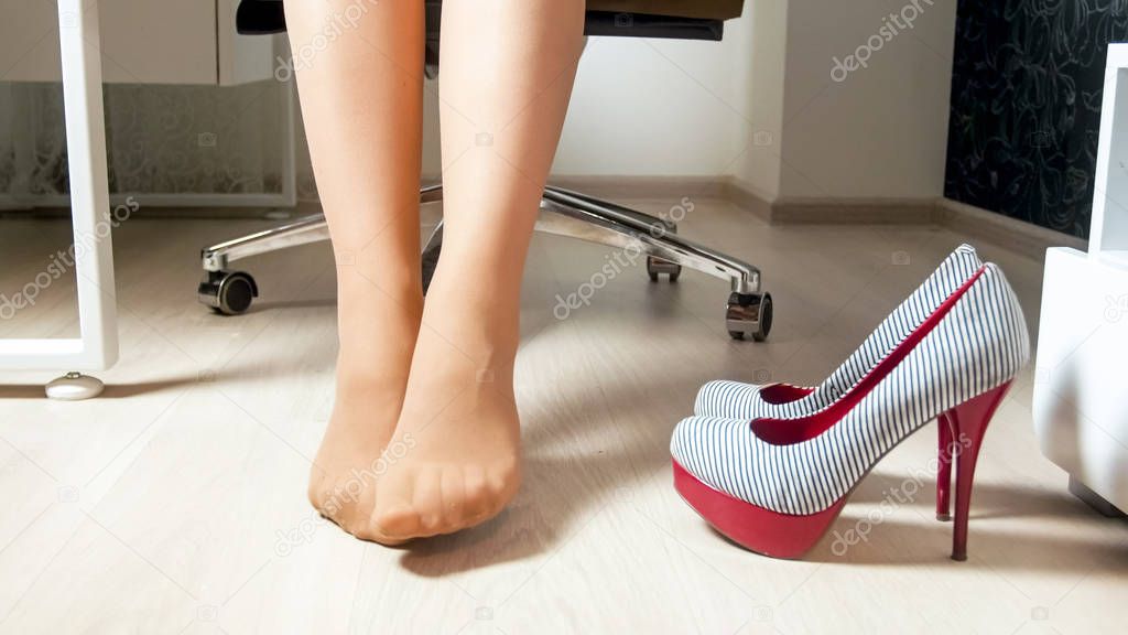 Closeup image of young businesswoman stretching tired legs in office