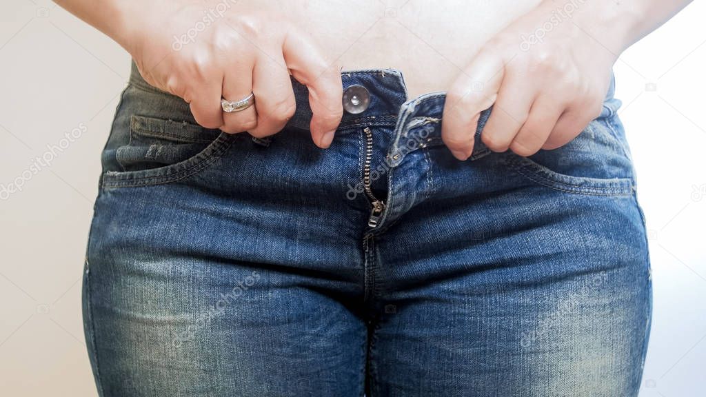 Closeup image of young woman buttoning tight jeans