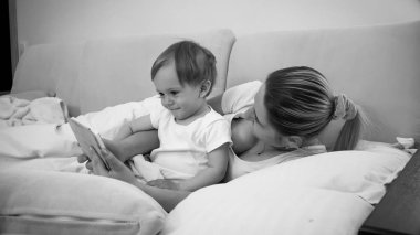 Siyah beyaz görüntü bir anne bebek oğluyla dijital tablet ile yatakta yalan