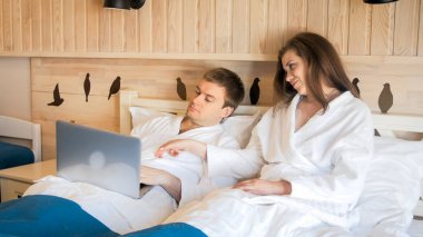 Dizüstü bilgisayarda çalışan adam ile yatakta yatan genç kadın