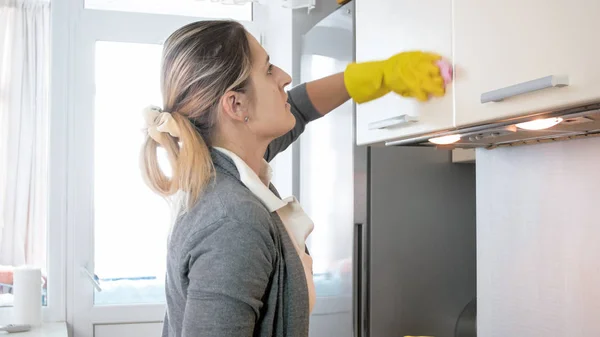 Hermosa mujer rubia joven limpiando armarios sucios en la cocina —  Fotos de Stock