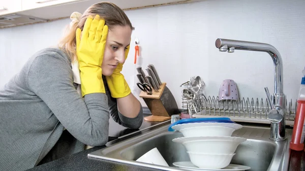 Портрет втомленої молодої жінки, яка дивиться на купу брудного посуду — стокове фото