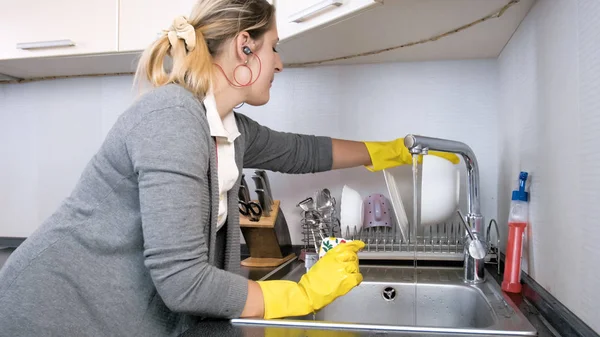 Porträt einer jungen Hausfrau in gelben Gummihandschuhen, die Musik hört und Geschirr spült — Stockfoto