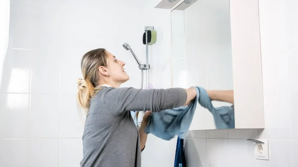 Portrait of beautiful young woman cleaning mirror with cloth — Stock Photo, Image