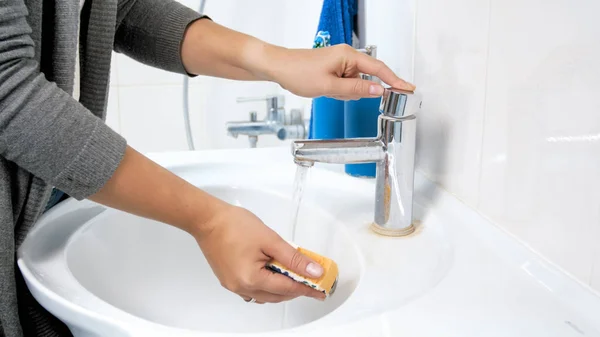 Foto di primo piano della giovane donna che versa acqua sulla spugna gialla prima di fare pulizia — Foto Stock