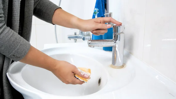 Foto de primer plano de la joven empapando esponja amarilla con agua antes de hacer la limpieza en el baño —  Fotos de Stock