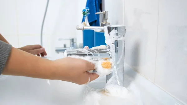 Foto de primer plano de una mujer joven que aplica detergente en una esponja amarilla para regar el grifo y el lavabo —  Fotos de Stock