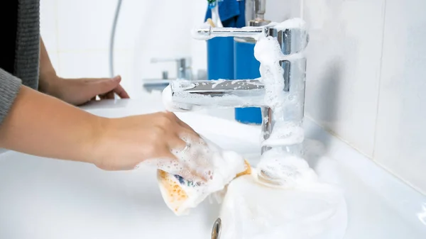 Foto close-up de jovem mulher segurando esponja embebida com detergente suds lavatório pia do banheiro — Fotografia de Stock