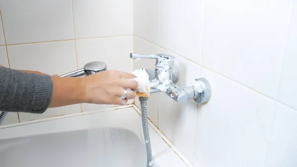 Крупный план молодой женщины чистящей воду кран в ванной комнате с моющим средством — стоковое фото