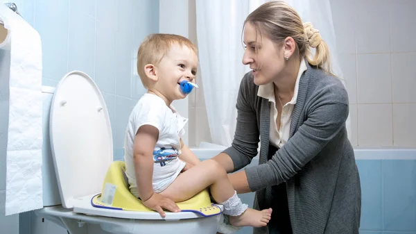 Madre joven sentando a su hijo pequeño asiento especial para niños toiilet — Foto de Stock