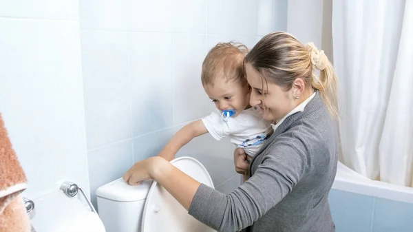 Молодая мать со своим малышом смывает воду в унитаз после использования — стоковое фото