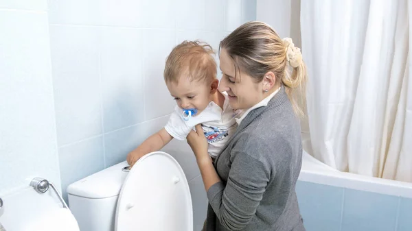 Portré, fiatal anya bemutatja a kisgyermek fia, hogy WC öblítő gomb segítségével — Stock Fotó