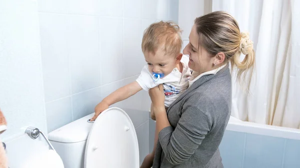 Fiatal anya kisgyermek fia, aki a WC öblítő gomb megnyomásával — Stock Fotó