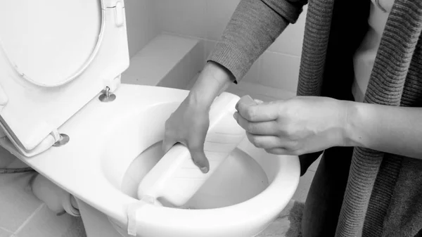 Closeup black and white photo of young woman pouring detergent in toilet — Stock Photo, Image