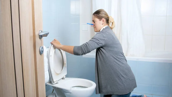 Jonge vrouw met wasknijper op neus reinigen van toilet thuis — Stockfoto