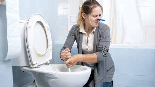 Портрет брезгливой молодой женщины, чистящей туалет щеткой — стоковое фото