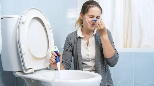 Портрет брезгливой молодой женщины, надевающей прищепку на нос перед мытьем туалета — стоковое фото