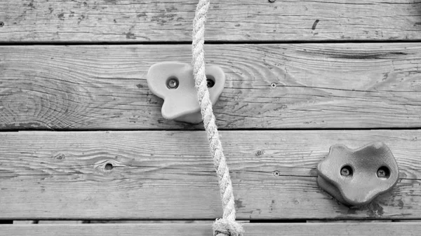 Black and white closeup image of wooden wall with rope and rocks for climbing — Stock Photo, Image