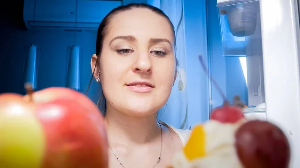 Портрет крупным планом изнутри холодильника ночью женщины, смотрящей на еду на полках — стоковое фото