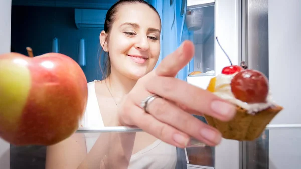Nahaufnahme einer hungrigen jungen Frau, die süßen Kuchen aus dem Kühlschrank nimmt — Stockfoto