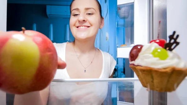 Retrato de cerca de una mujer joven sintió hambre por la noche tomando manzana del refrigerador —  Fotos de Stock