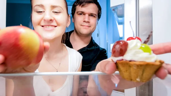 Retrato de cerca de la familia joven tomando manzana y pastel del refrigerador por la noche —  Fotos de Stock