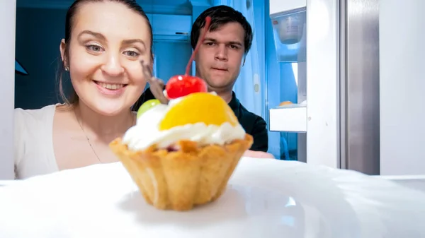 Retrato desde el interior del refrigerador de pareja hambrienta mirando pastel dulce —  Fotos de Stock