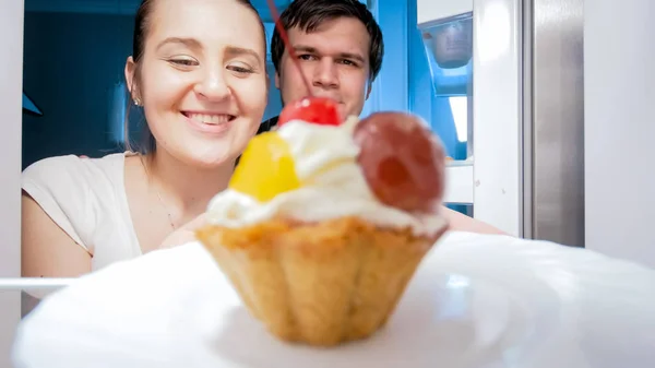 Portrait from inside of refrigerator of young couple looking on cake — Stock Photo, Image