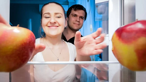 Retrato de família jovem feliz que toma maçãs do refrigerador à noite — Fotografia de Stock