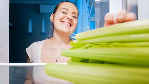 Blick aus dem Inneren des Kühlschranks auf eine junge Frau, die Sellerie nimmt — Stockfoto